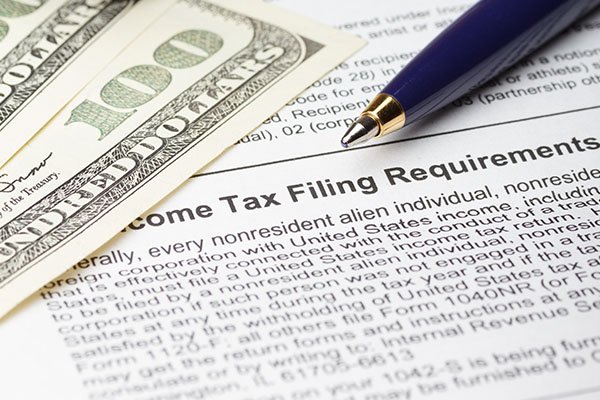 Tax filing requirements document with U.S. dollars and a pen, representing USTax101’s nonresident tax filing services.